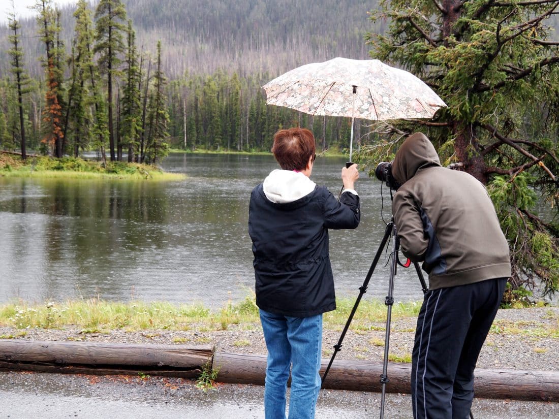 Image of a women holding umbrella over photographer head while taking photos of small lake in pouring rain
